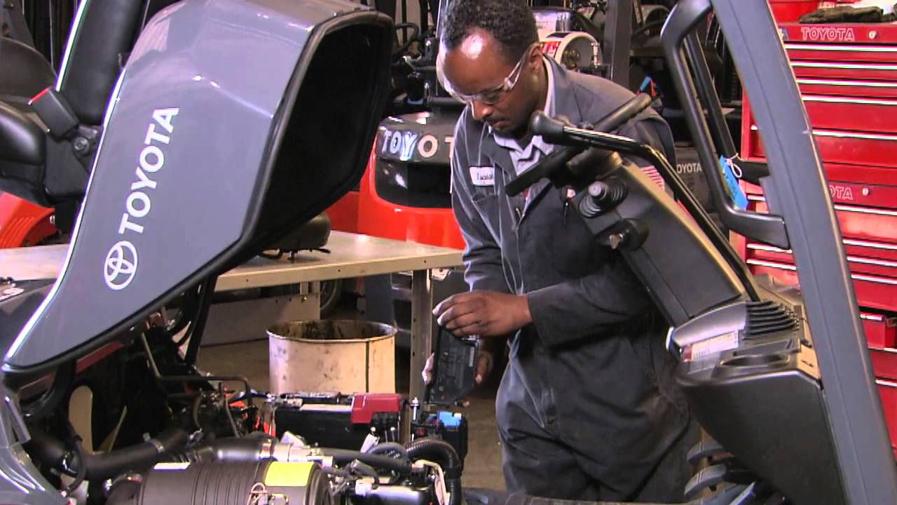 Male technician working on forklift engine in warehouse.