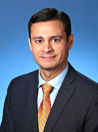 Retrato profesional de un hombre blanco con una chaqueta de traje negro y corbata naranja sobre un fondo azul