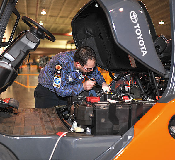 Male technician working on forklift engine in warehouse.