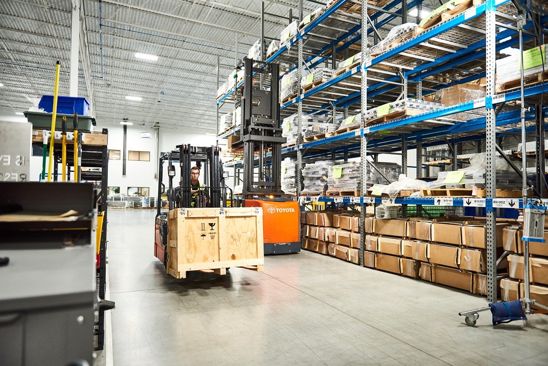 Man drives Toyota forklift with wooden crate across warehouse