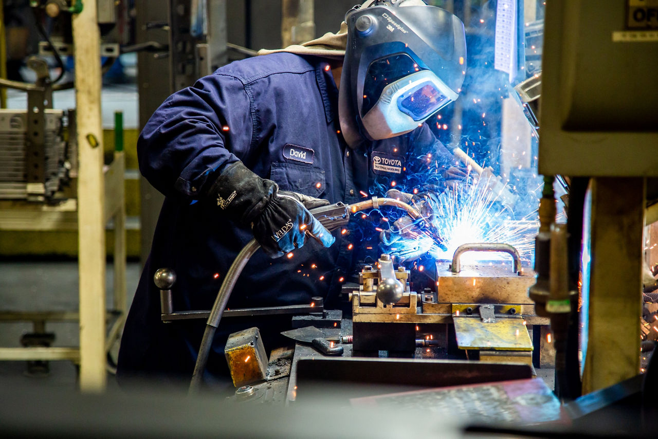 toyota welding associate with hard hat on welding a piece of equipment