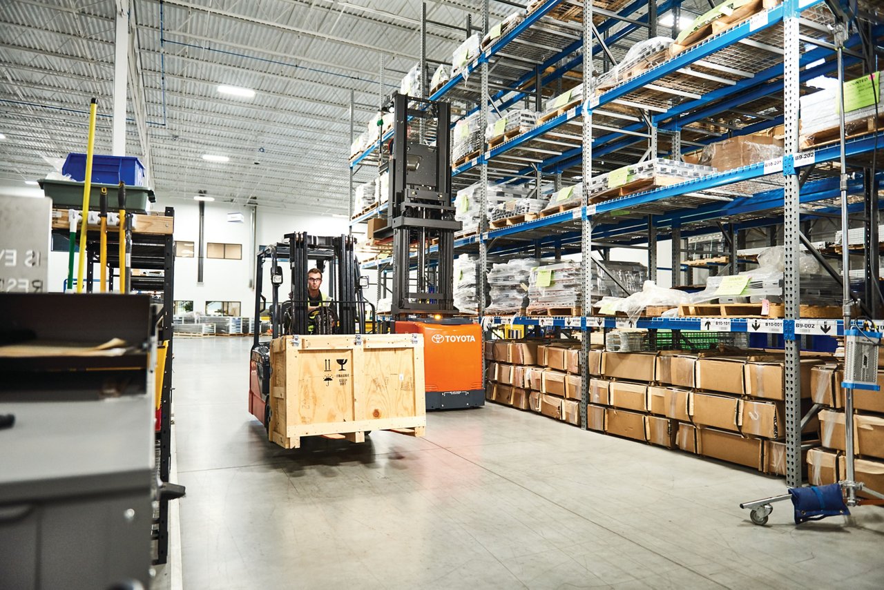Man driving forklift in warehouse while it carries wooden crate