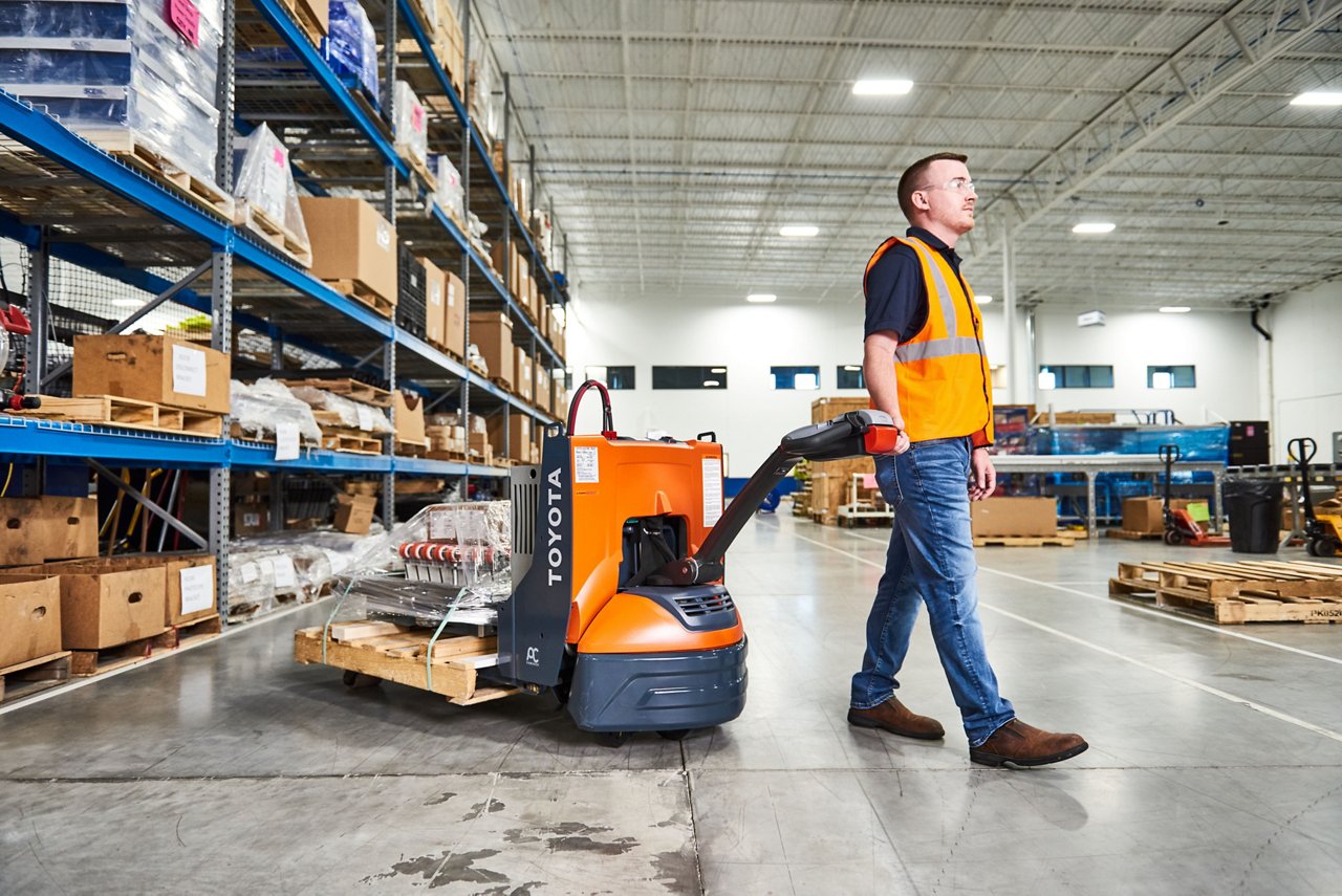Man using an electric walkie to carry materials across warehouse 