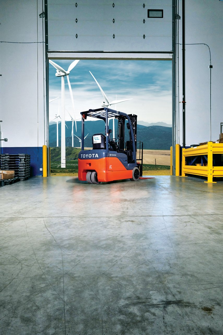 Toyota forklift parked in warehouse in front of open garage, with a view of electric windmills in the background 