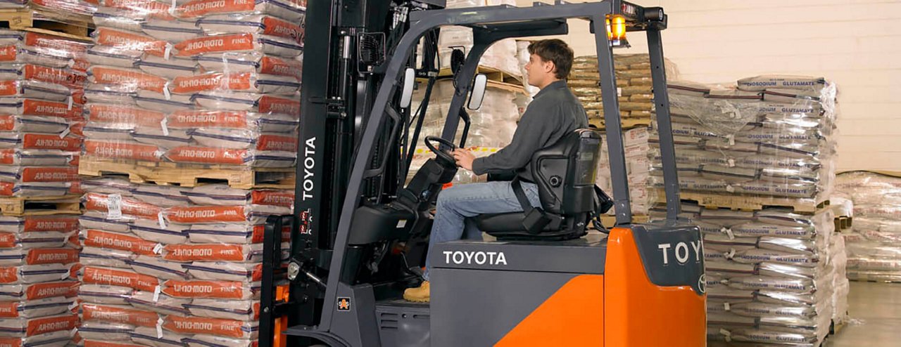 Man uses Toyota forklift to pick up many bags of material in warehouse 