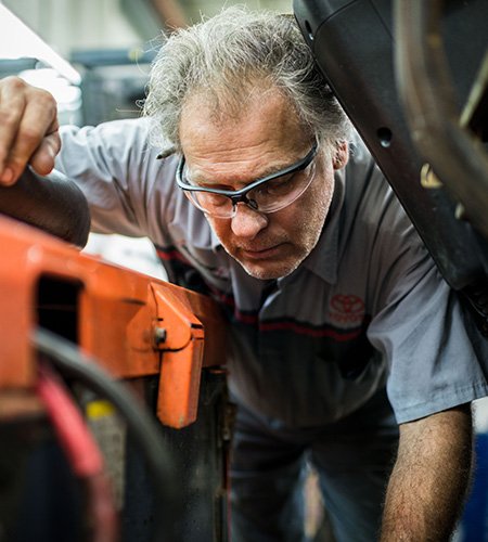 forklift technician looking into a forklift currently under repair